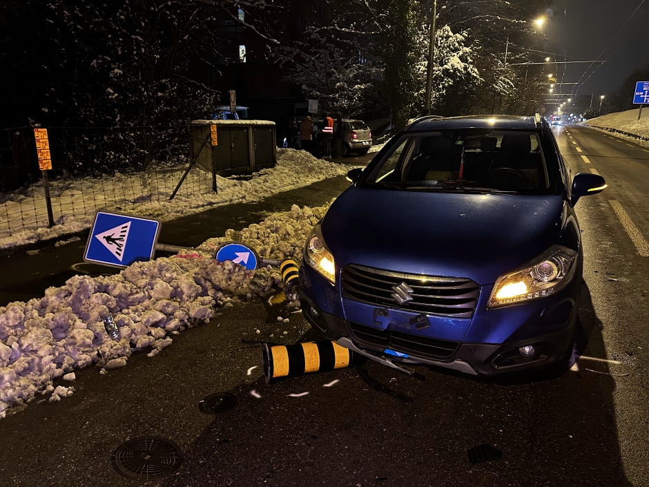 Ein blaues Auto steht nach einem Unfall auf einer verschneiten Strasse. Der Vorderteil des Autos ist besch&auml;digt. Ein Verkehrsteiler wurde von einem weiteren Autofahrer umgefahren und liegt auf der Strasse..